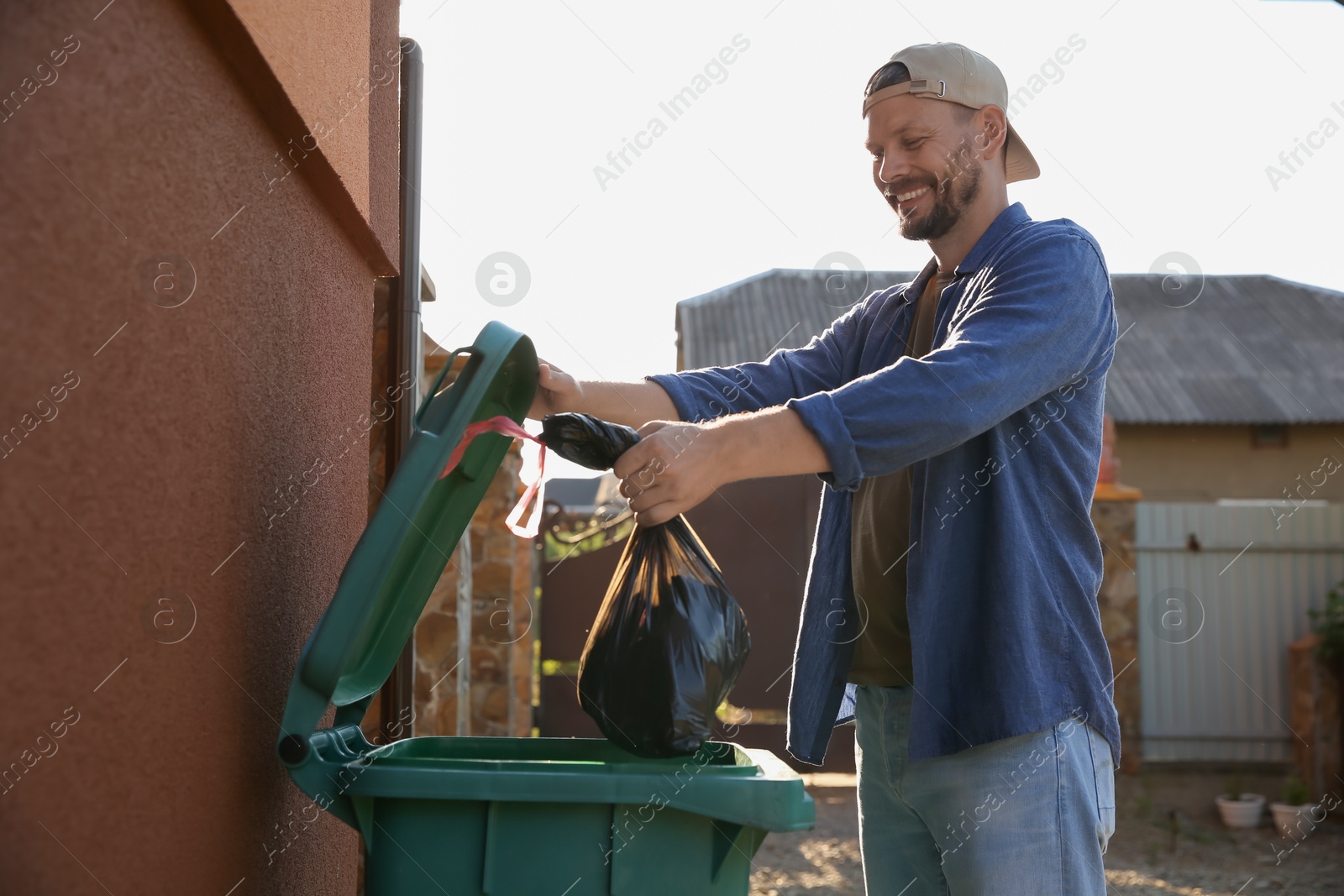 Photo of Man throwing trash bag full of garbage into bin outdoors