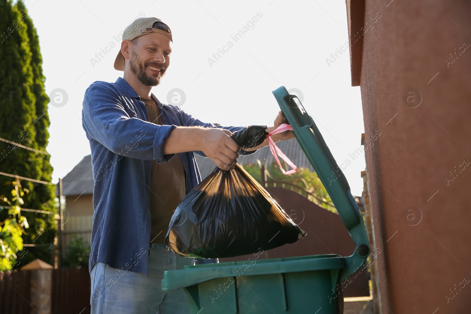 Photo of Man throwing trash bag full of garbage into bin outdoors