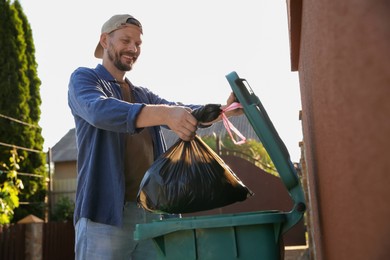 Photo of Man throwing trash bag full of garbage into bin outdoors