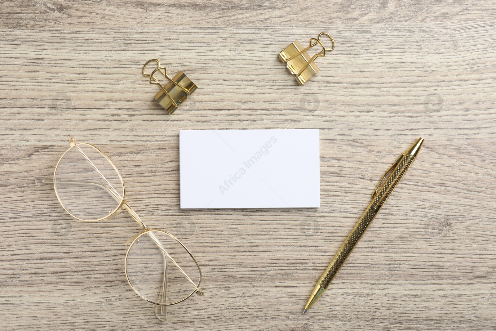 Photo of Blank business cards, glasses, golden pen and binder clips on wooden table, flat lay. Mockup for design