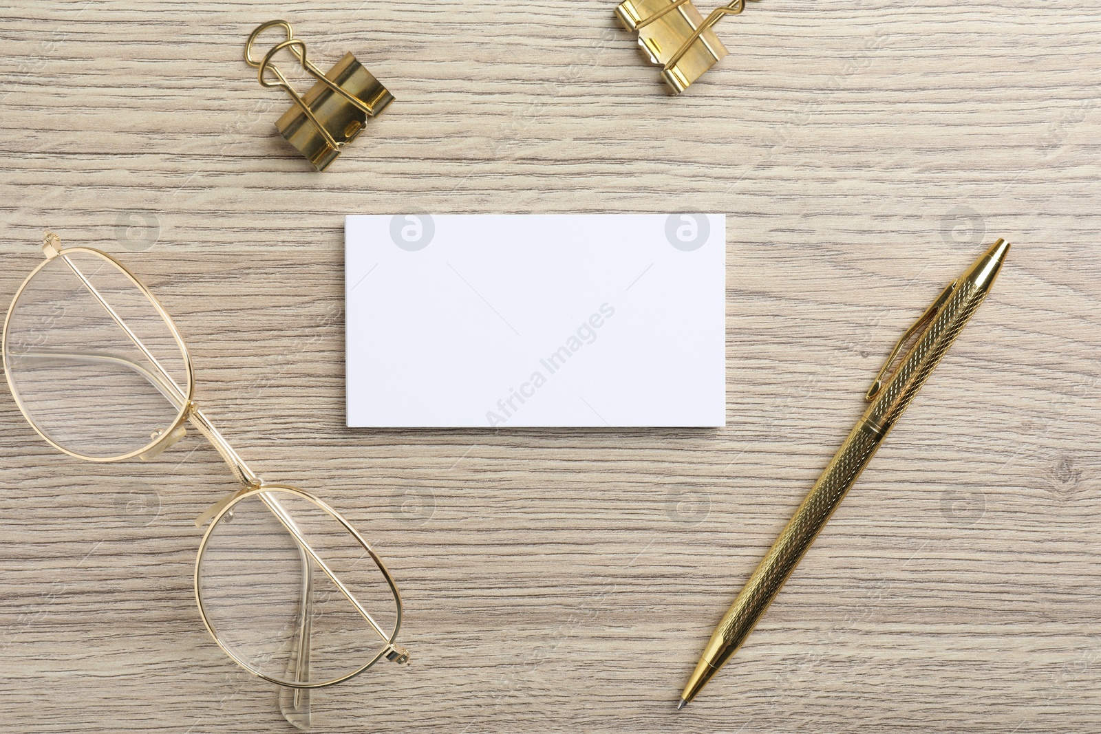 Photo of Blank business cards, glasses, golden pen and binder clips on wooden table, flat lay. Mockup for design