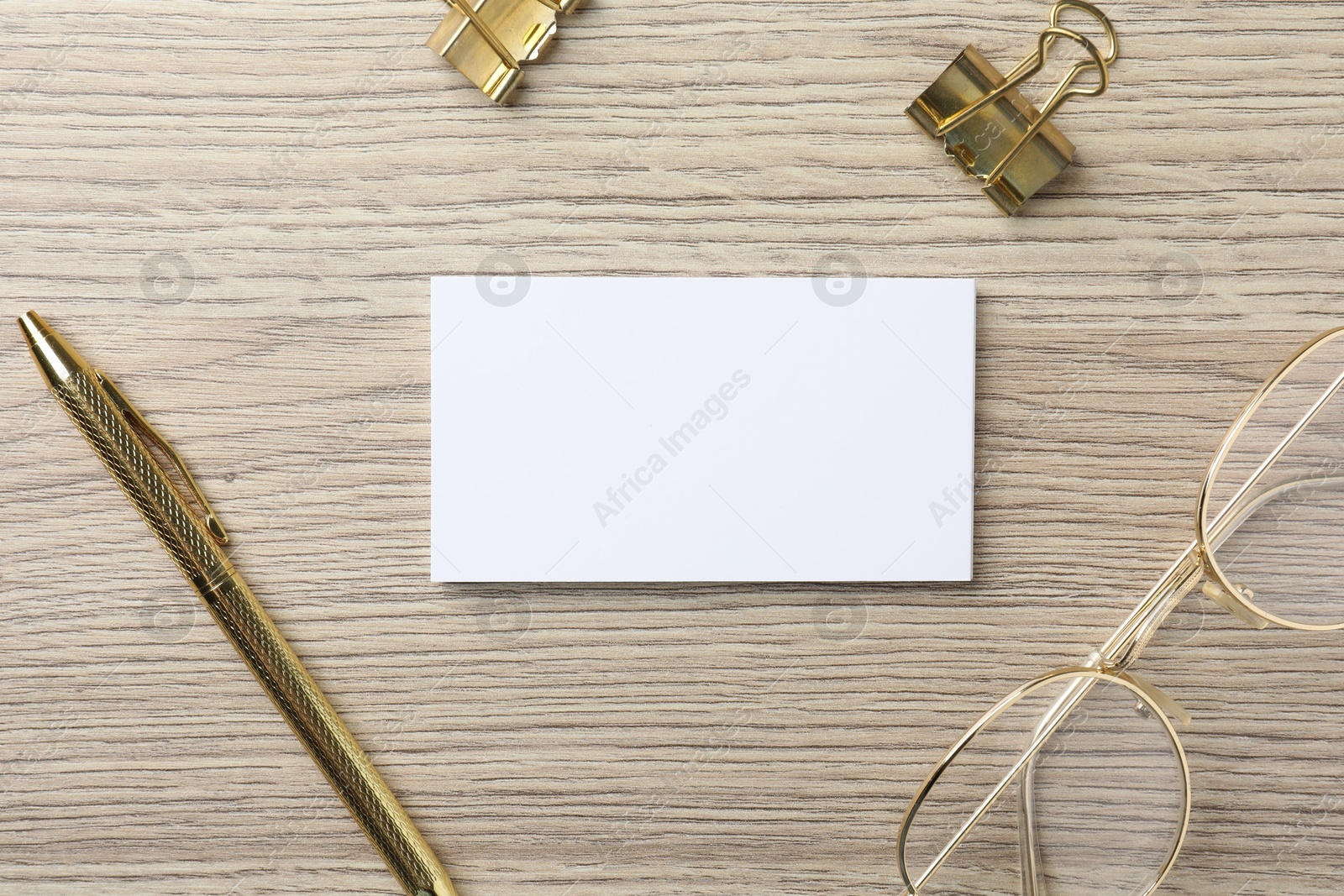 Photo of Blank business cards, glasses, golden pen and binder clips on wooden table, flat lay. Mockup for design