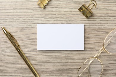 Photo of Blank business cards, glasses, golden pen and binder clips on wooden table, flat lay. Mockup for design