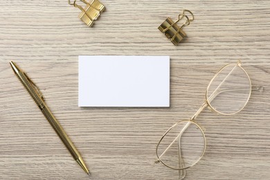 Photo of Blank business cards, glasses, golden pen and binder clips on wooden table, flat lay. Mockup for design