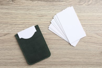 Photo of Leather card holder with blank business cards on wooden table, flat lay. Mockup for design