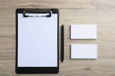 Blank business cards, clipboard with sheet and pen on wooden table, flat lay. Mockup for design