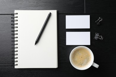 Photo of Blank business cards, notebook, pen, coffee and binder clips on black wooden table, flat lay. Mockup for design