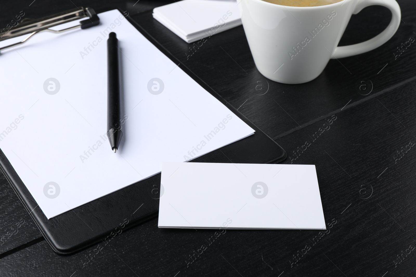 Photo of Blank business cards, clipboard with sheet, pen and cup on black wooden table. Mockup for design