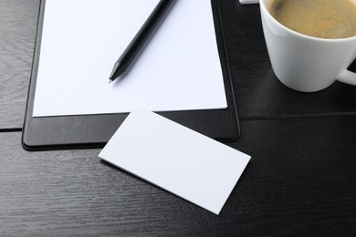 Photo of Blank business cards, clipboard with sheet, pen and cup on black wooden table. Mockup for design