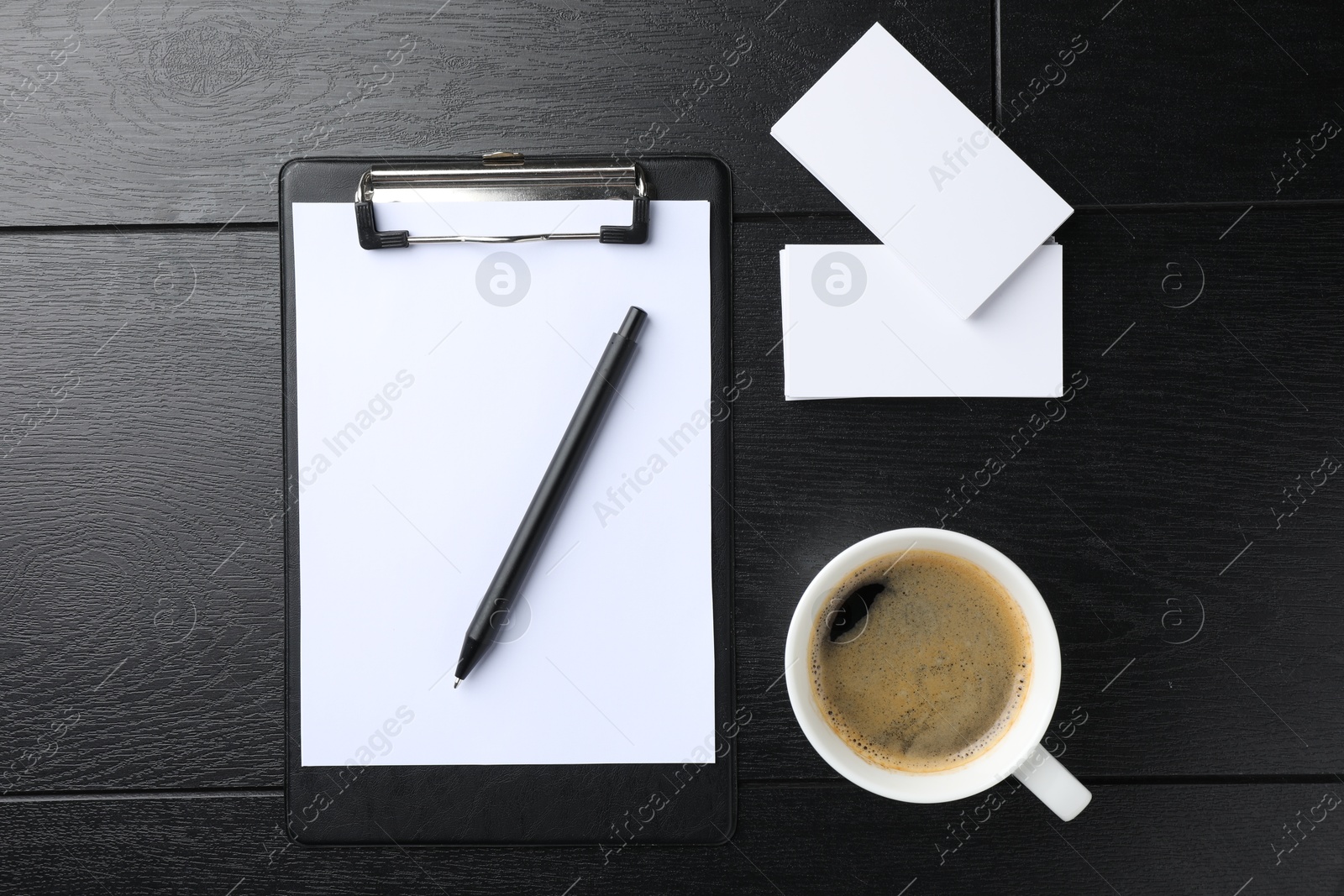 Photo of Blank business cards, clipboard with sheet, pen and coffee on black wooden table, flat lay. Mockup for design