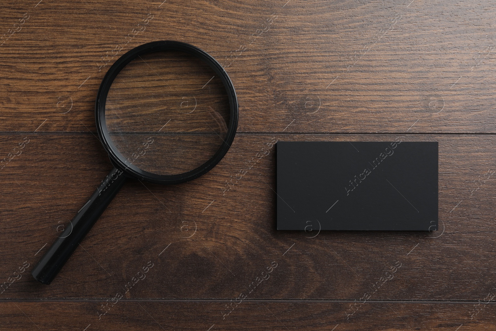 Photo of Blank business cards and magnifying glass on wooden table, flat lay. Mockup for design