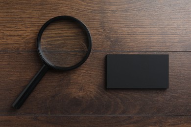 Blank business cards and magnifying glass on wooden table, flat lay. Mockup for design