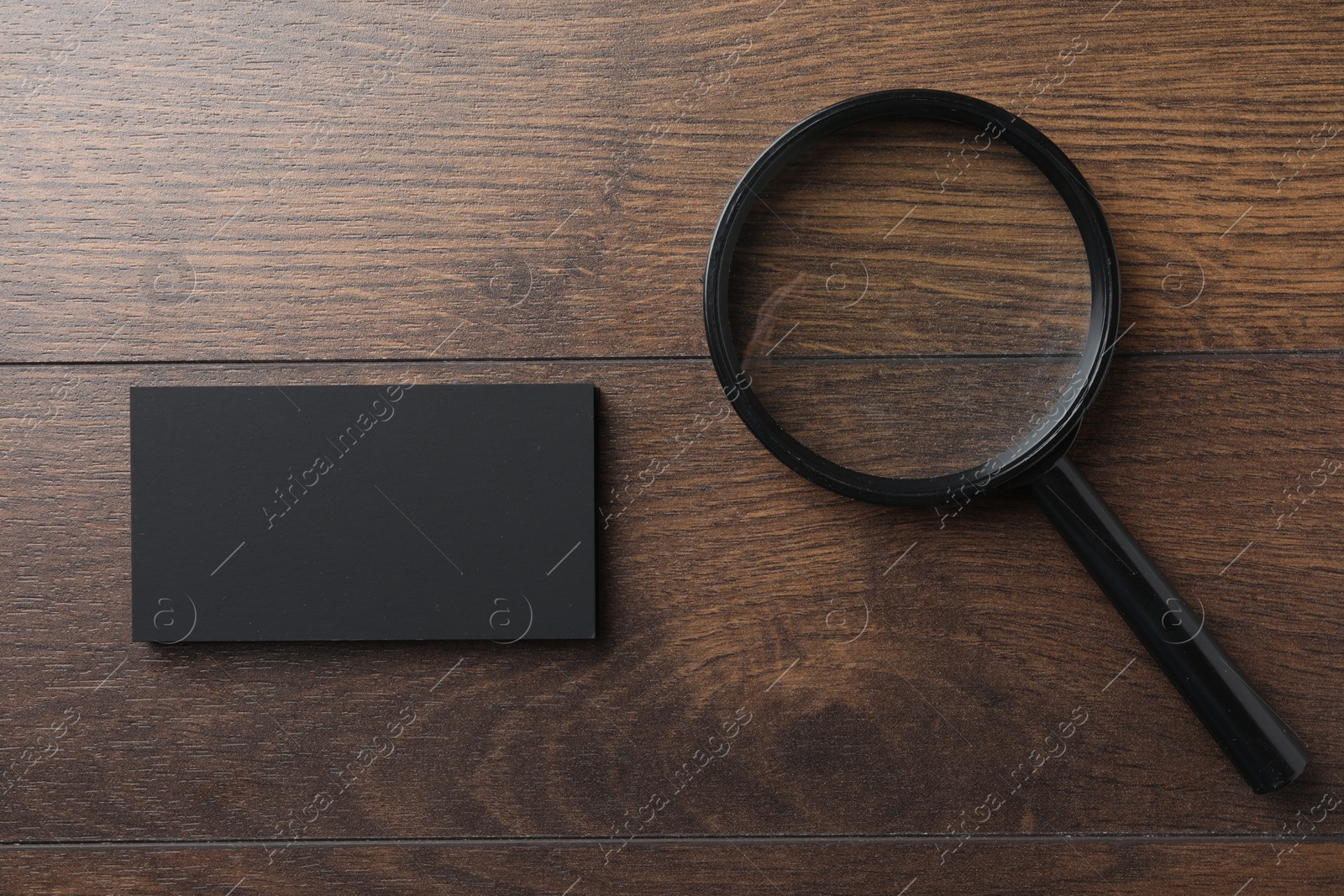 Photo of Blank business cards and magnifying glass on wooden table, flat lay. Mockup for design