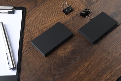 Photo of Blank business cards, clipboard with sheet, pen and binder clips on wooden table. Mockup for design