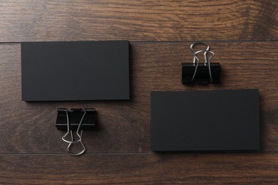 Blank business cards and binder clips on wooden table, flat lay. Mockup for design