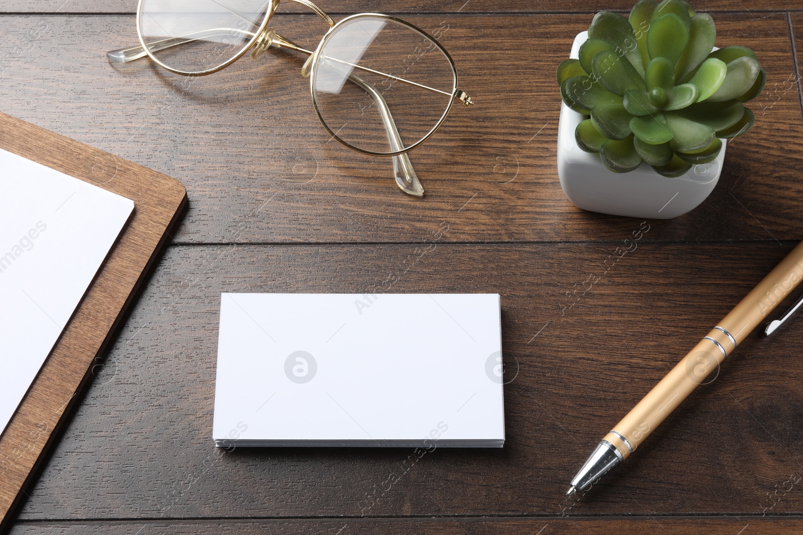 Photo of Blank business cards, clipboard with sheet, plant, glasses and pen on wooden table. Mockup for design