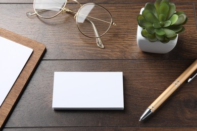 Blank business cards, clipboard with sheet, plant, glasses and pen on wooden table. Mockup for design