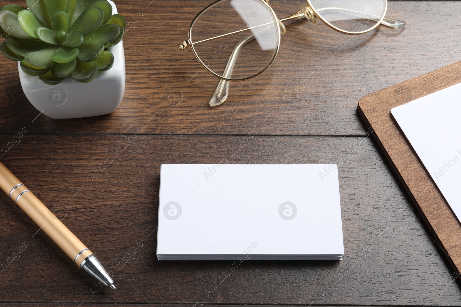 Photo of Blank business cards, clipboard with sheet, plant, glasses and pen on wooden table. Mockup for design