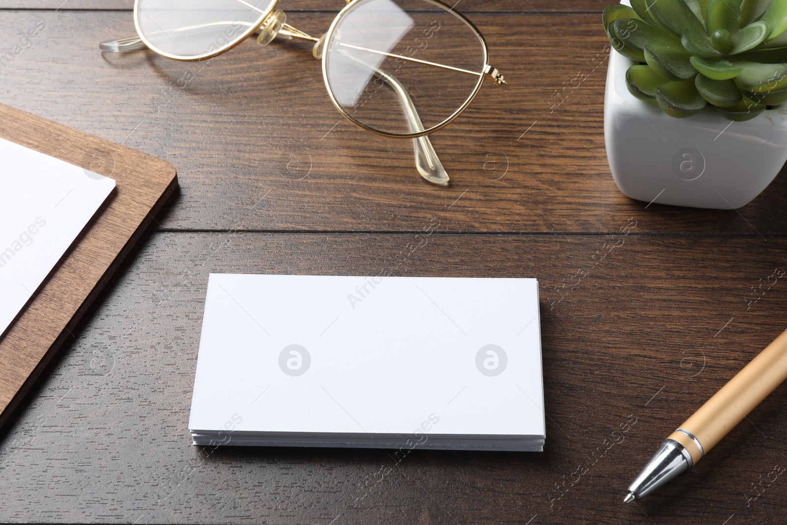 Photo of Blank business cards, clipboard with sheet, plant, glasses and pen on wooden table. Mockup for design