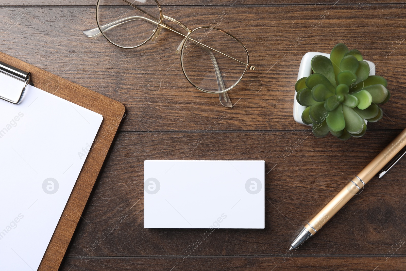 Photo of Blank business cards, clipboard with sheet, plant, glasses and pen on wooden table, flat lay. Mockup for design