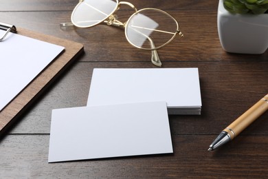 Blank business cards, clipboard with sheet, glasses and pen on wooden table. Mockup for design