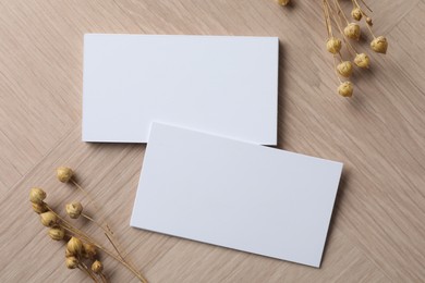 Photo of Blank business cards and dried herbs on wooden table, flat lay. Mockup for design