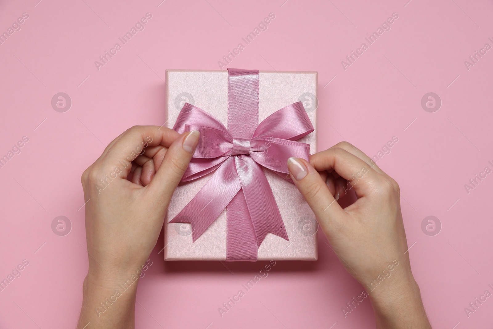 Photo of Woman decorating gift box with bow on pink background, top view