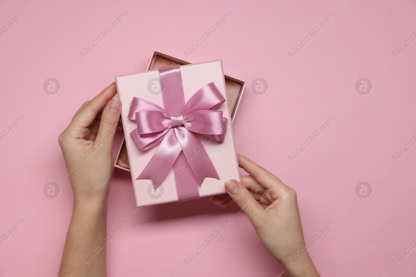 Photo of Woman decorating gift box with bow on pink background, top view