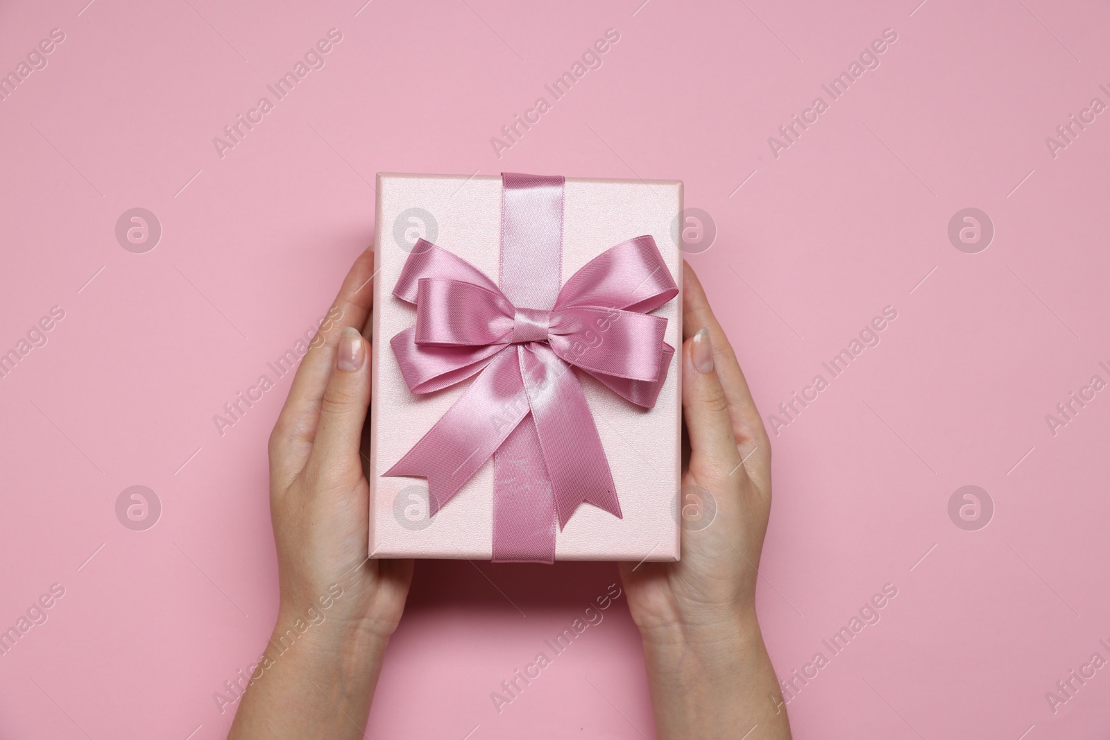 Photo of Woman holding gift box with bow on pink background, top view