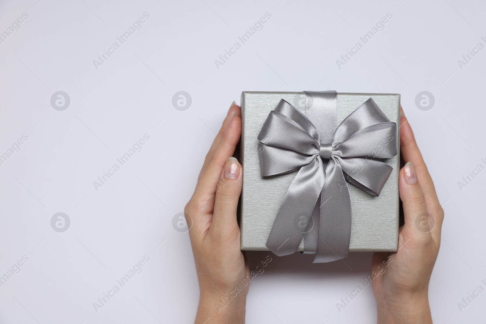 Photo of Woman holding gift box with bow on white background, top view. Space for text