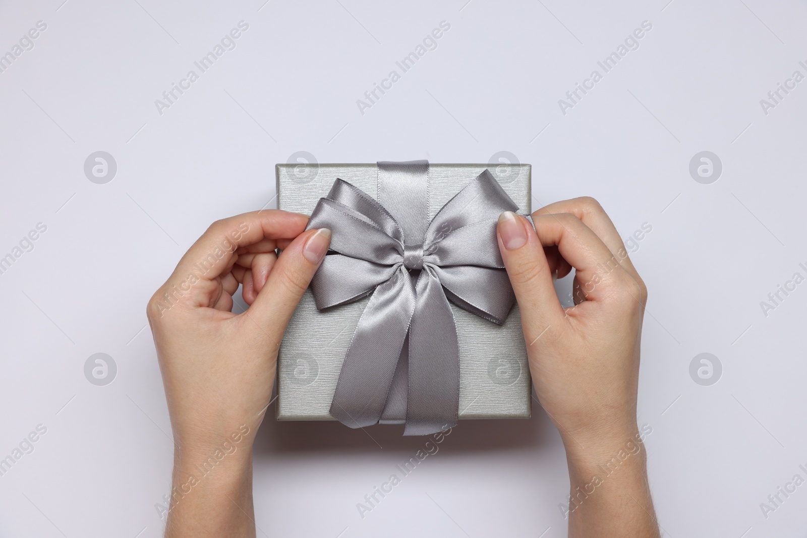 Photo of Woman decorating gift box with bow on white background, top view