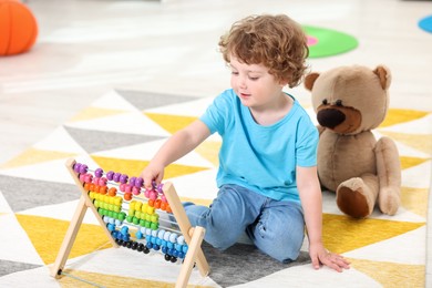 Photo of Cute little boy playing with wooden abacus on floor in kindergarten