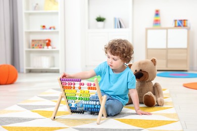 Cute little boy playing with wooden abacus on floor in kindergarten