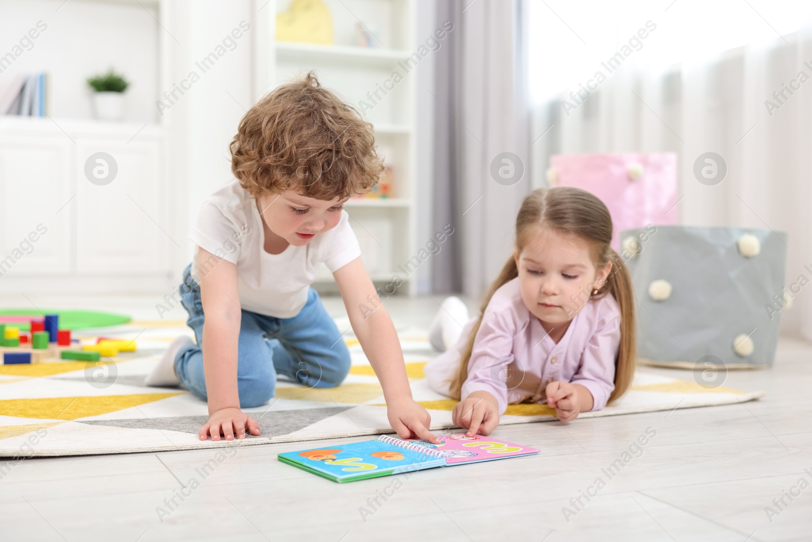 Photo of Cute little children reading book on floor in kindergarten