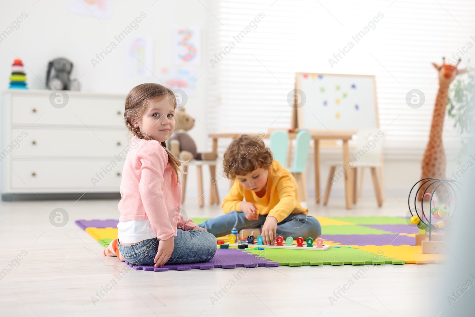 Photo of Cute little children playing together on puzzle mat in kindergarten