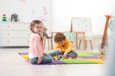 Cute little children playing together on puzzle mat in kindergarten