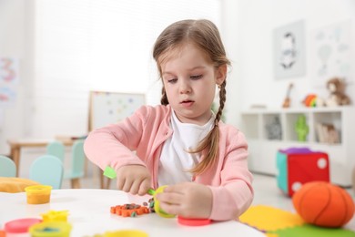 Photo of Cute little girl modeling from plasticine at white table in kindergarten