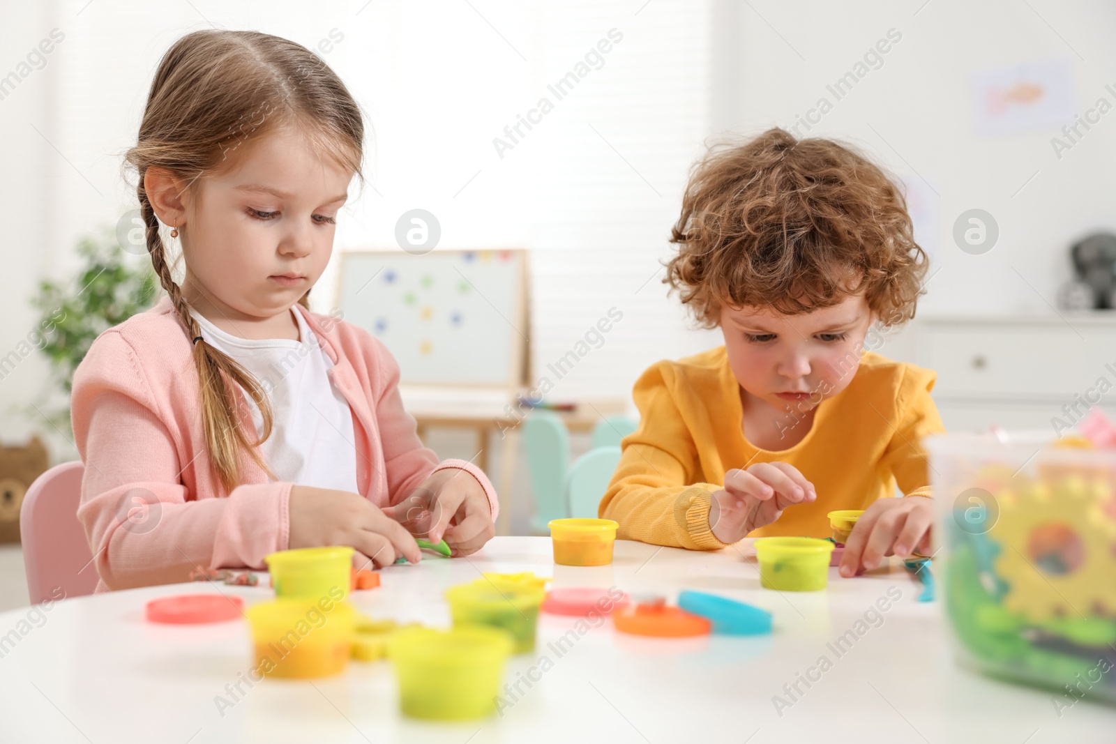 Photo of Cute little children modeling from plasticine at white table in kindergarten