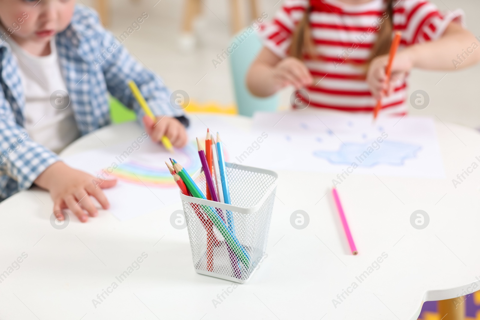 Photo of Little children drawing with colorful pencils at white table in kindergarten, selective focus