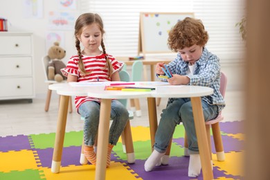 Cute little children drawing with colorful pencils at white table in kindergarten