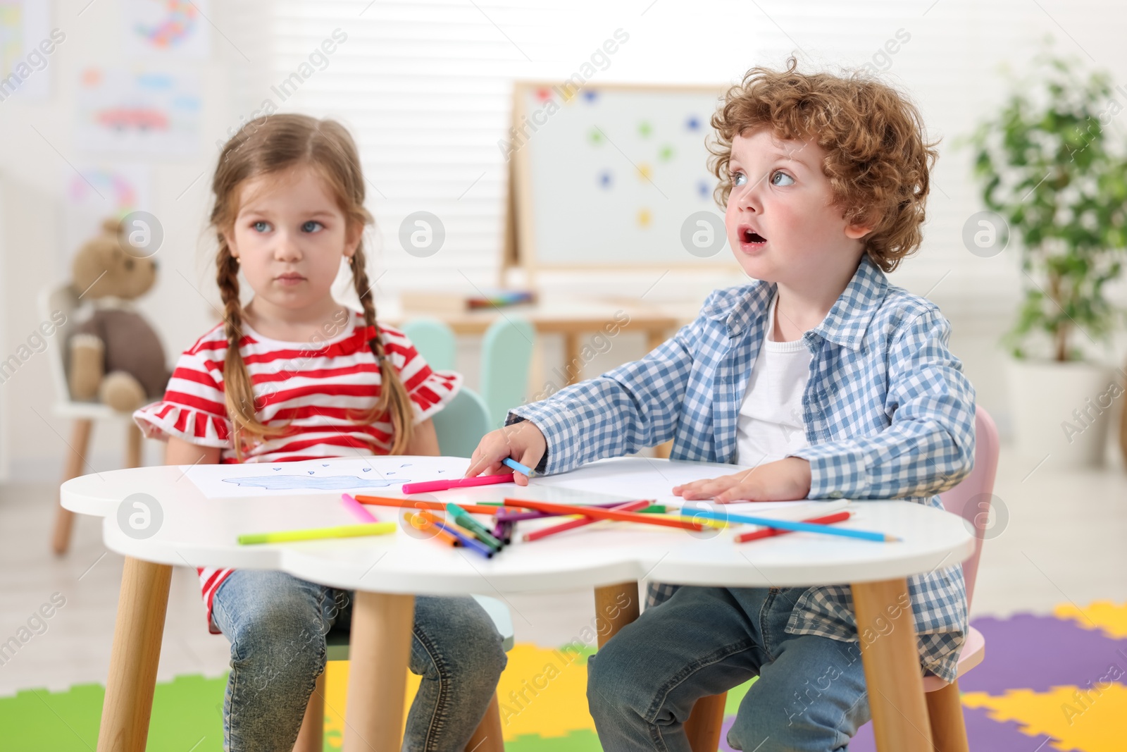 Photo of Cute little children drawing with colorful pencils at white table in kindergarten