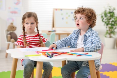 Cute little children drawing with colorful pencils at white table in kindergarten