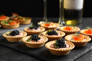 Photo of Delicious canapes with salmon and caviar on black textured table, closeup