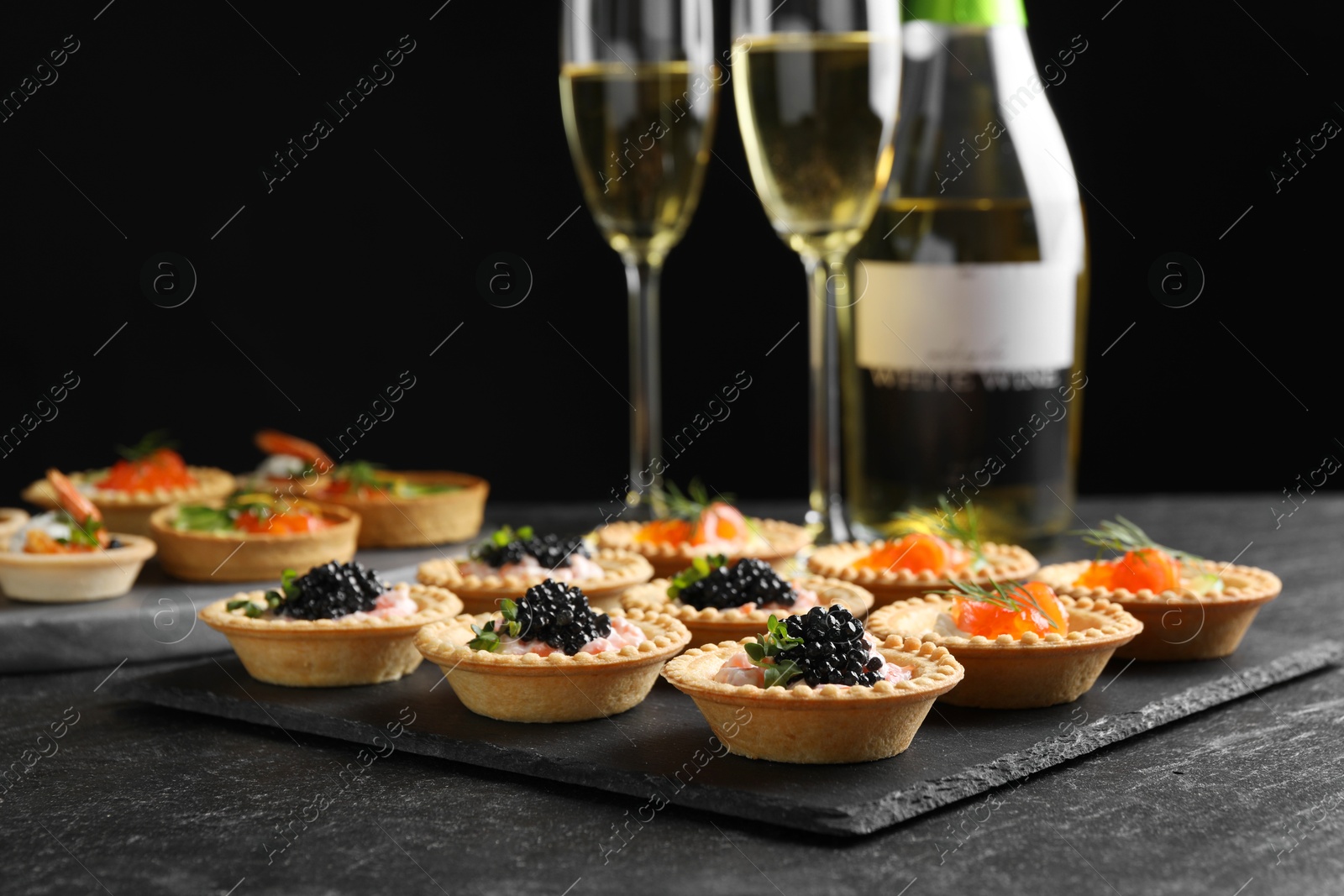 Photo of Delicious canapes with salmon and caviar on black textured table, closeup