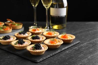 Photo of Delicious canapes with salmon and caviar on black textured table, closeup