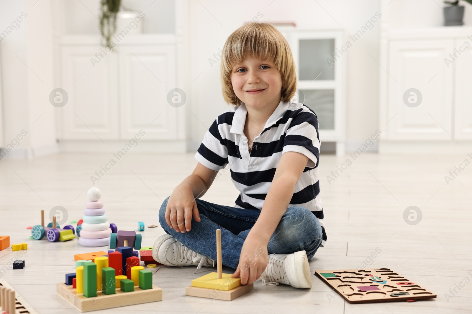 Photo of Cute little boy playing with toy pyramid on floor indoors