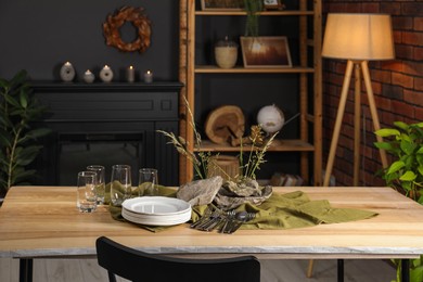 Clean dishes, stones and plants on wooden table in stylish dining room