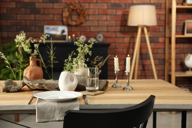 Photo of Set of clean dishware, vases with beautiful flowers, stones and burning candles on wooden table in stylish dining room