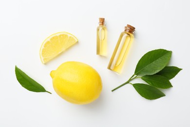 Photo of Bottles of essential oils, lemon and green leaves on white background, flat lay