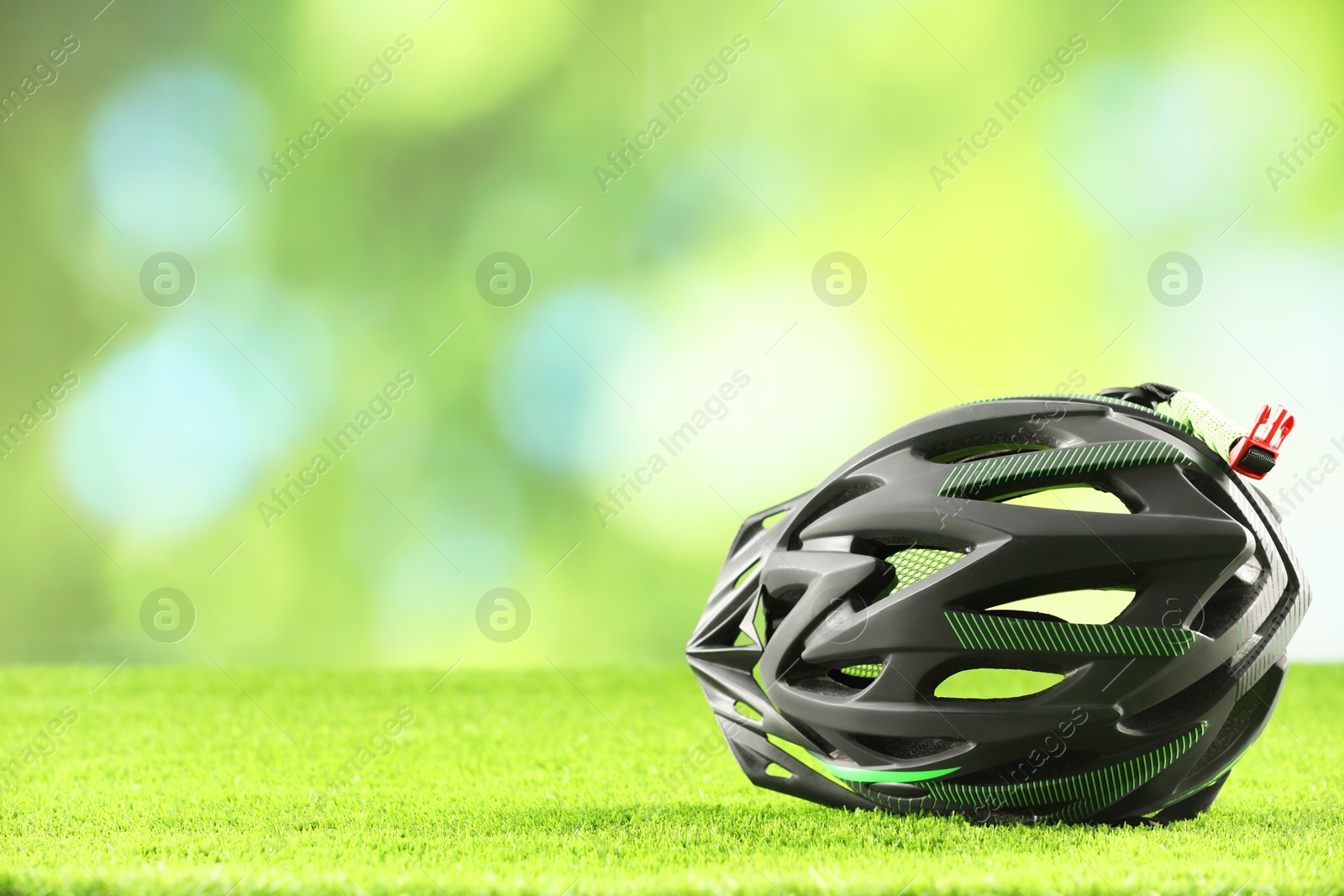 Photo of Stylish protective helmet on green grass against blurred background. Space for text